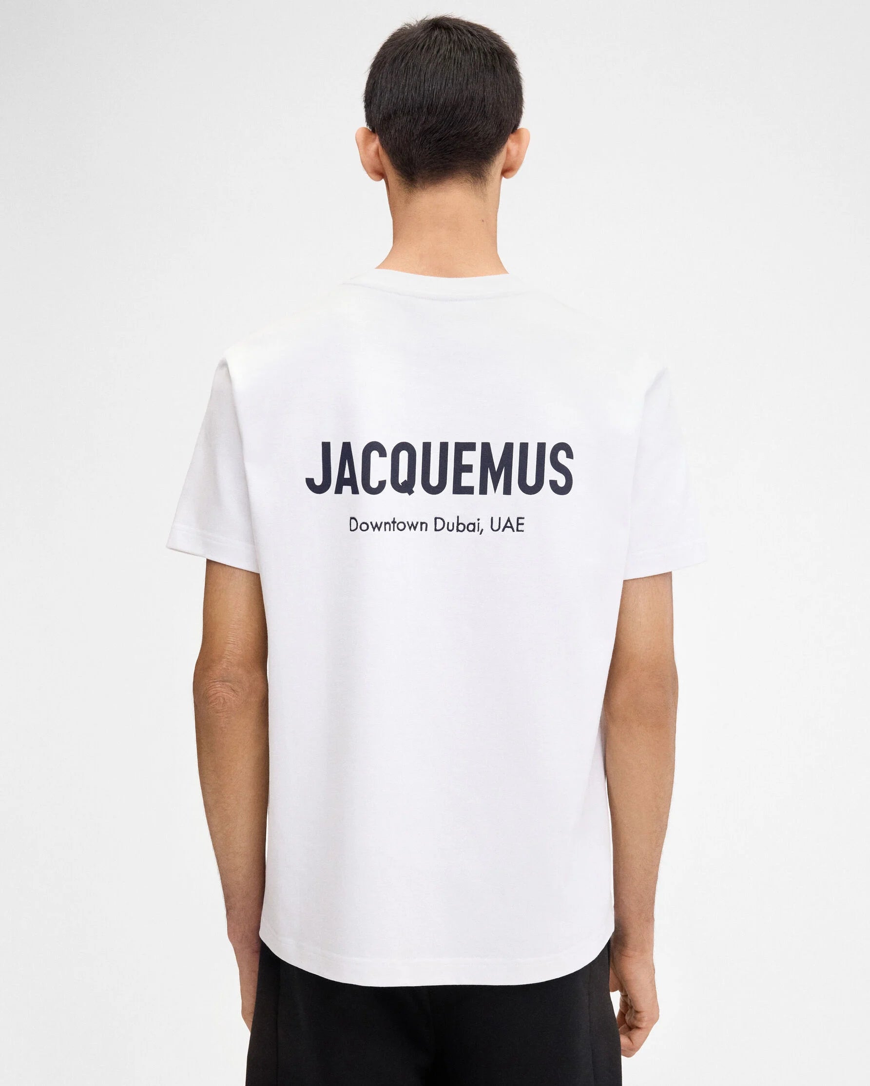 TEE SHIRT JACQUEMUS BLANC AVEC LOGO IMPRIME EN NOIR SUR LE COEUR A L'AVANT AINSI QU'ECRIS JACQUEMUS EN GROS DANS LE DOS ET AVEC UNE ADRESSE EN PLUS PETIT JUSTE EN DESSOUS