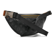 Louis Vuitton Discovery Bumbag Monogram Eclipse Gaston Label Savane Yellow, sac banane Monogram noir et gris avec détail jaune et finitions argentées.