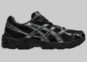 Image de l’ASICS GEL-1130 Black/Pure Silver – sneaker noire en mesh et cuir synthétique avec détails argentés métallisés, insert GEL® visible au talon. (vue de profil)