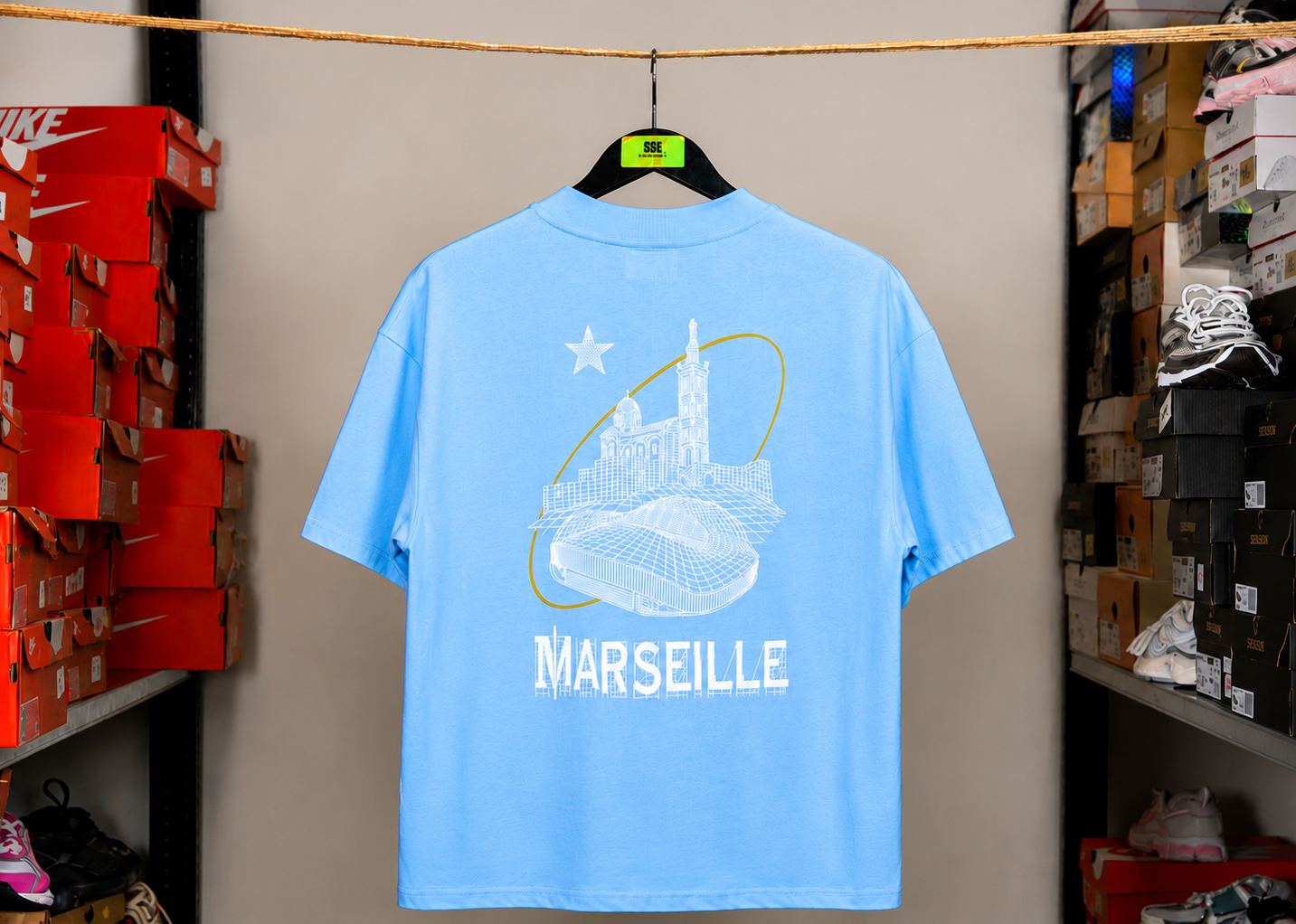 T-shirt Global Sneakers Marseille 2026 bleu ciel en coton premium 240 g/m² fabriqué en Italie, avec logo brodé sur la poitrine et sérigraphie exclusive de Notre-Dame de la Garde et du stade Vélodrome au dos.