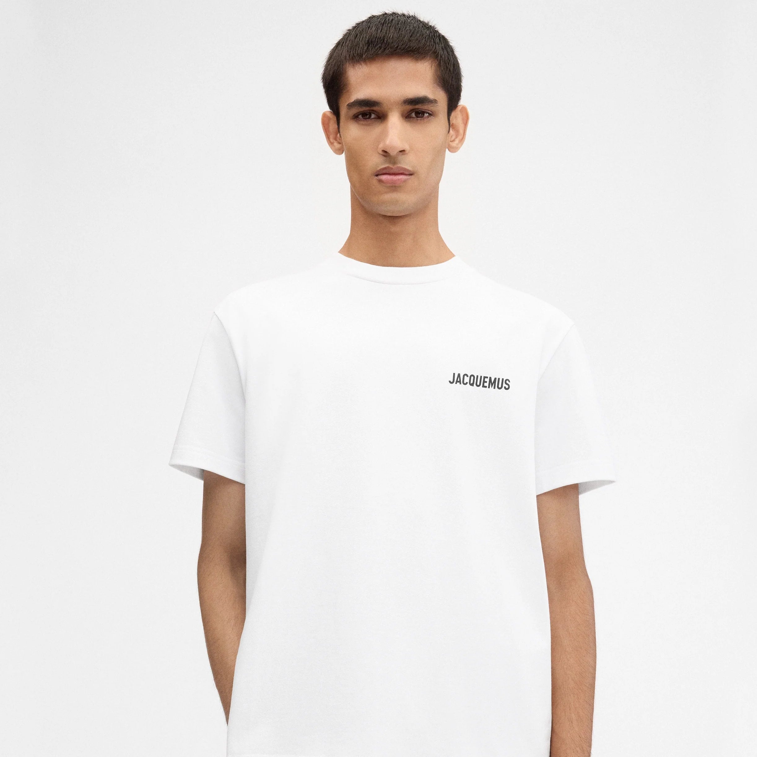 TEE SHIRT JACQUEMUS BLANC AVEC LOGO IMPRIME EN NOIR SUR LE COEUR A L'AVANT AINSI QU'ECRIS JACQUEMUS EN GROS DANS LE DOS ET AVEC UNE ADRESSE EN PLUS PETIT JUSTE EN DESSOUS