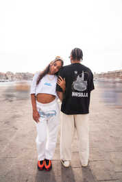 T-shirt noir Global Sneakers x Ailleurs/Higher Marseille – sérigraphie blanche et dorée avec monuments marseillais", porter par 2 mannequins tshirt noir et tshirt blanc et bleu