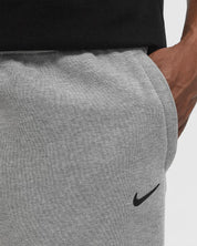Nike x NOCTA Fleece CS Sweatpant Dark Grey Heather, pantalon fleece gris chiné avec poignets côtelés, poches zippées et détails NOCTA.
