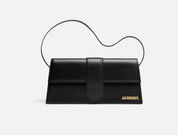 Jacquemus Le Bambino Long Shoulder Bag Black, sac d’épaule en cuir noir lisse avec rabat structuré, silhouette allongée et logo doré.