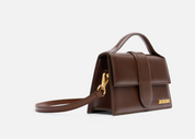 Jacquemus Le Grand Bambino Crossbody Flap Bag Dark Brown, sac en cuir marron foncé structuré avec rabat, poignée et détails dorés.
