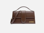 Jacquemus Le Grand Bambino Crossbody Flap Bag Dark Brown, sac en cuir marron foncé structuré avec rabat, poignée et détails dorés.