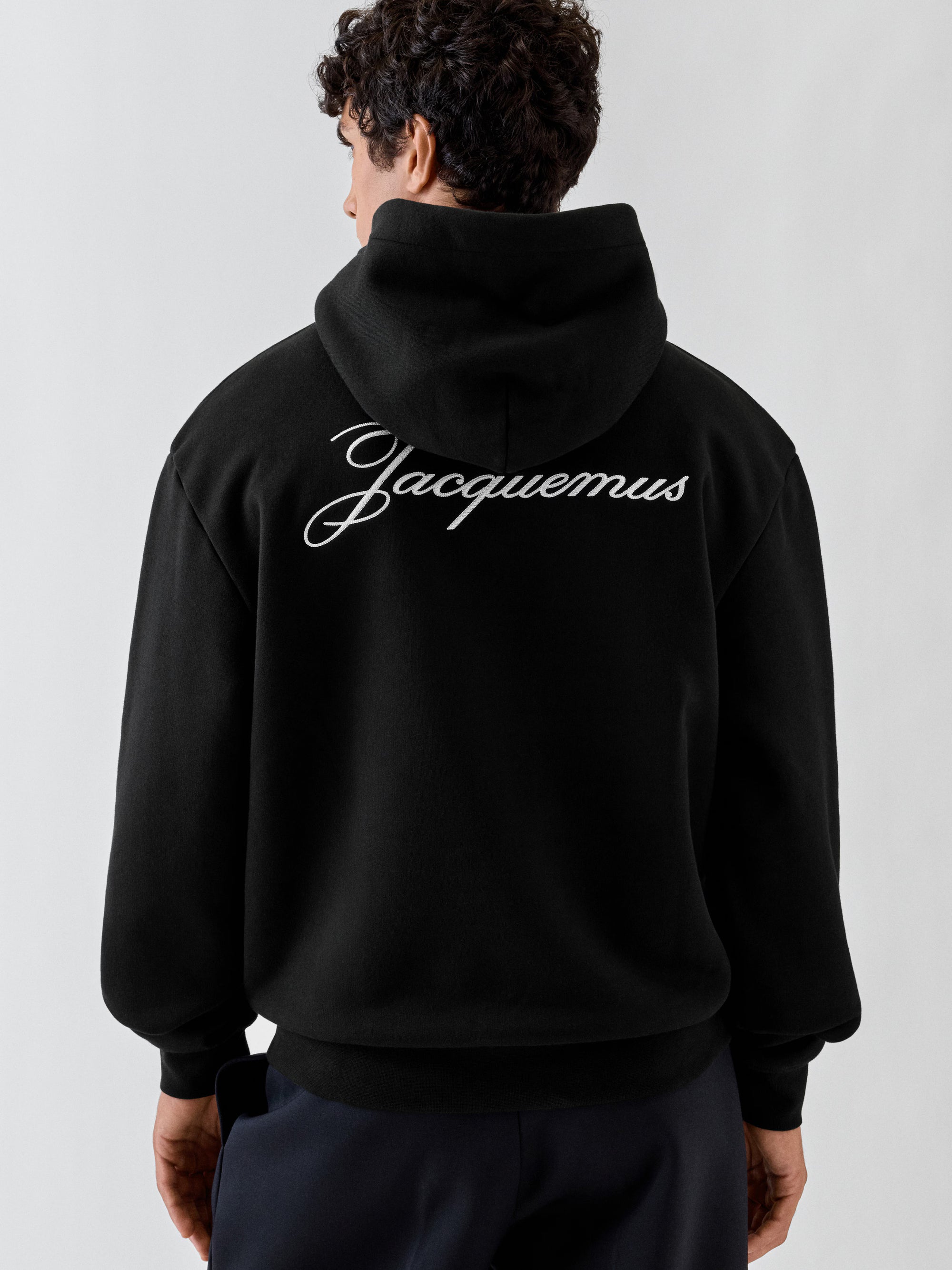 Jacquemus Le Hoodie Logo Brodé en coton molletonné avec coupe ample, petit logo J brodé sur la poitrine et signature Jacquemus au dos.