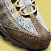 Vue zoomée sur les détails avants de la Nike Air Max 95 NH Ironstone en tons brun, taupe et Olive Grey avec panneaux en textile jacquard, détails Celery et unités Air-Sole visibles.