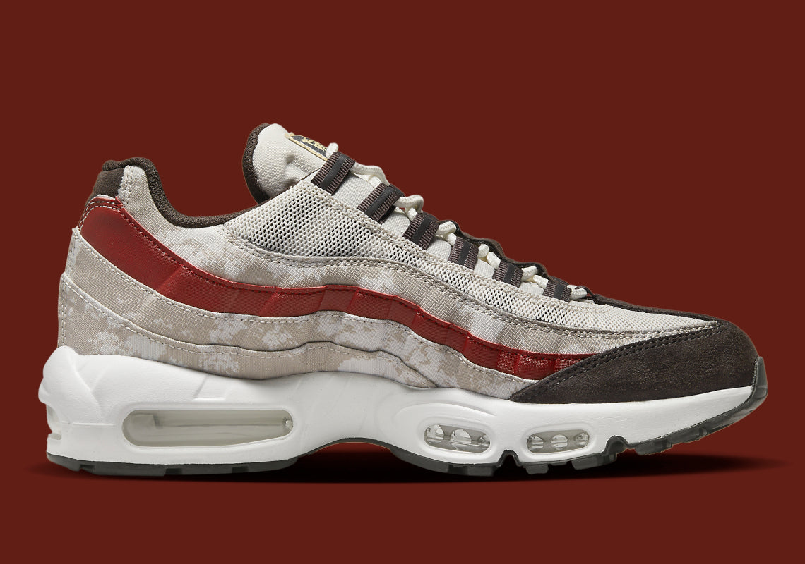 Nike Air Max 95 Social FC DQ9016-001, sneaker beige, marron et bordeaux avec motif camouflage, écusson football et unités Nike Air visibles.