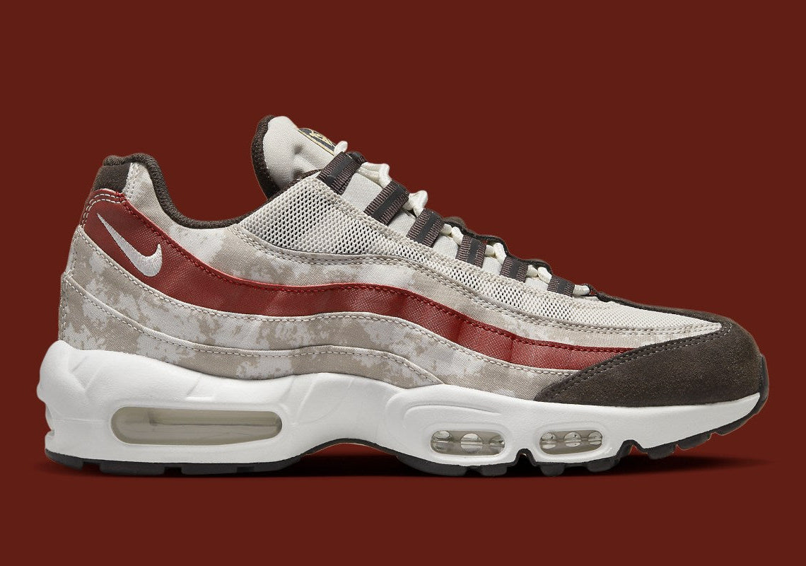 Nike Air Max 95 Social FC DQ9016-001, sneaker beige, marron et bordeaux avec motif camouflage, écusson football et unités Nike Air visibles.