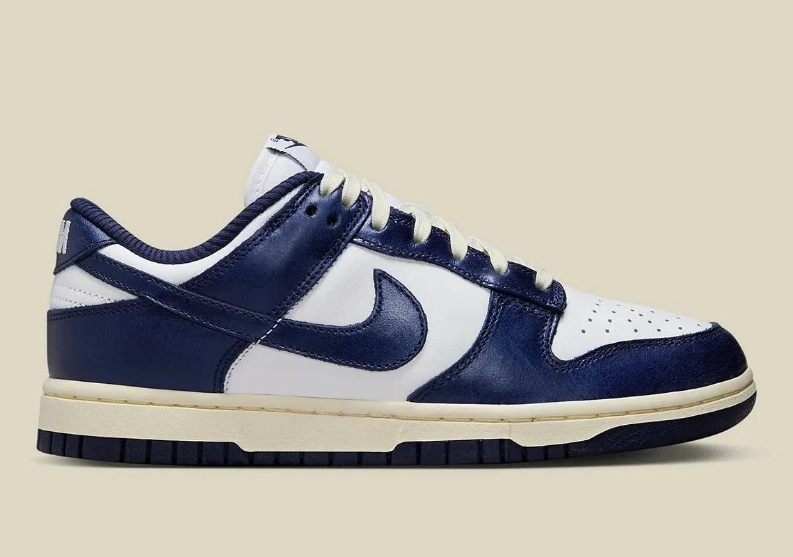 Nike Dunk Low PRM Vintage Navy, sneaker en cuir blanc et bleu marine avec Swoosh bleu et semelle crème effet vintage.