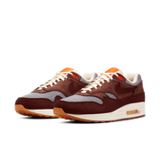 Image de la Nike Air Max 1 Houndstooth Bronze Eclipse, sneaker en mesh blanc cassé avec empiècements pied-de-poule, suede sable, détails Bronze Eclipse et unité Air visible.