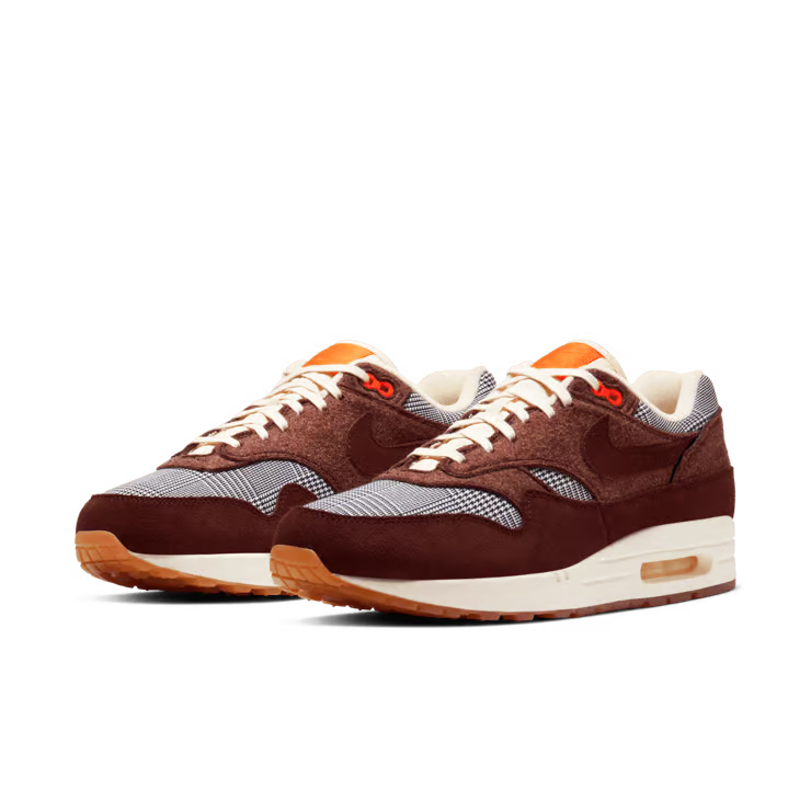 Image de la Nike Air Max 1 Houndstooth Bronze Eclipse, sneaker en mesh blanc cassé avec empiècements pied-de-poule, suede sable, détails Bronze Eclipse et unité Air visible.