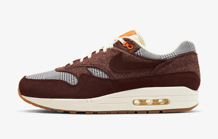 Image de la Nike Air Max 1 Houndstooth Bronze Eclipse, sneaker en mesh blanc cassé avec empiècements pied-de-poule, suede sable, détails Bronze Eclipse et unité Air visible.