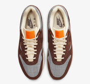 Image de la Nike Air Max 1 Houndstooth Bronze Eclipse, sneaker en mesh blanc cassé avec empiècements pied-de-poule, suede sable, détails Bronze Eclipse et unité Air visible.