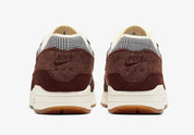 Image de la Nike Air Max 1 Houndstooth Bronze Eclipse, sneaker en mesh blanc cassé avec empiècements pied-de-poule, suede sable, détails Bronze Eclipse et unité Air visible.