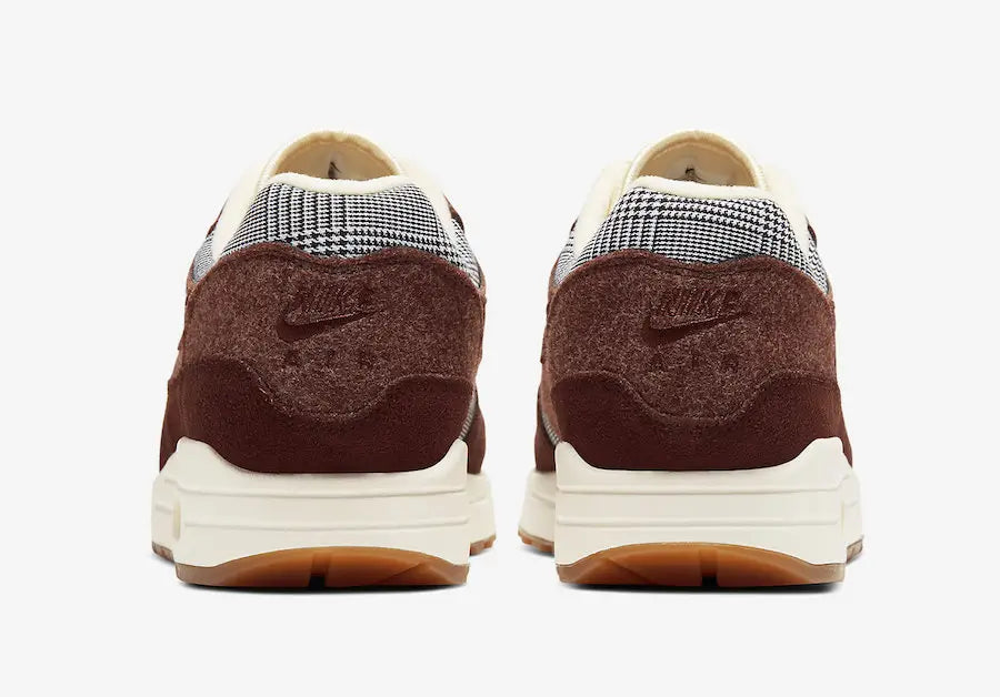 Image de la Nike Air Max 1 Houndstooth Bronze Eclipse, sneaker en mesh blanc cassé avec empiècements pied-de-poule, suede sable, détails Bronze Eclipse et unité Air visible.