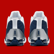 Nike Shox BB4 Olympics avec tige en cuir synthétique blanc et nubuck bleu marine, détails Metallic Silver, amorti Zoom Air à l'avant-pied et quatre colonnes Nike Shox au talon.