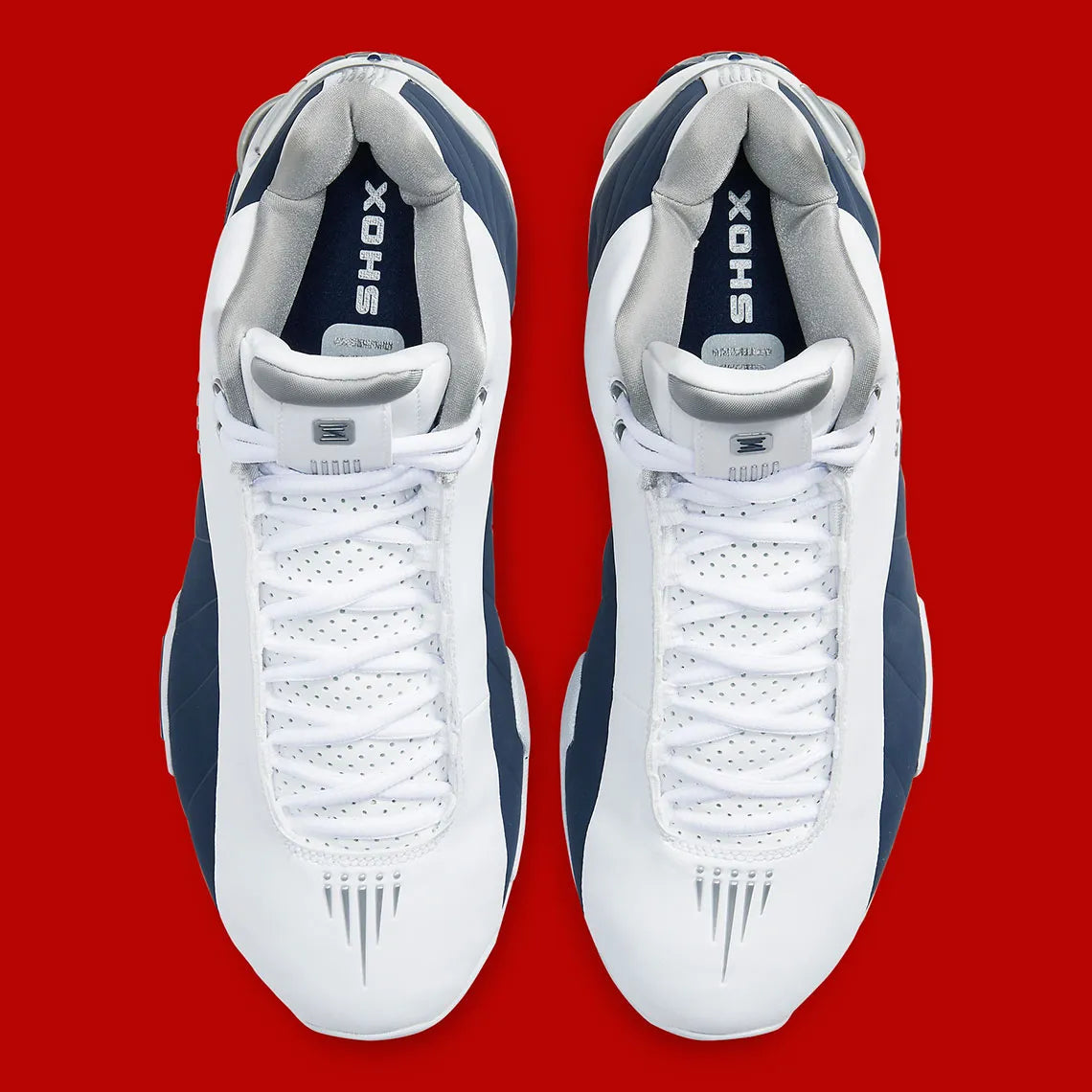 Nike Shox BB4 Olympics avec tige en cuir synthétique blanc et nubuck bleu marine, détails Metallic Silver, amorti Zoom Air à l'avant-pied et quatre colonnes Nike Shox au talon.