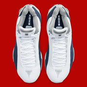Nike Shox BB4 Olympics avec tige en cuir synthétique blanc et nubuck bleu marine, détails Metallic Silver, amorti Zoom Air à l'avant-pied et quatre colonnes Nike Shox au talon.