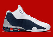 Nike Shox BB4 Olympics avec tige en cuir synthétique blanc et nubuck bleu marine, détails Metallic Silver, amorti Zoom Air à l'avant-pied et quatre colonnes Nike Shox au talon.