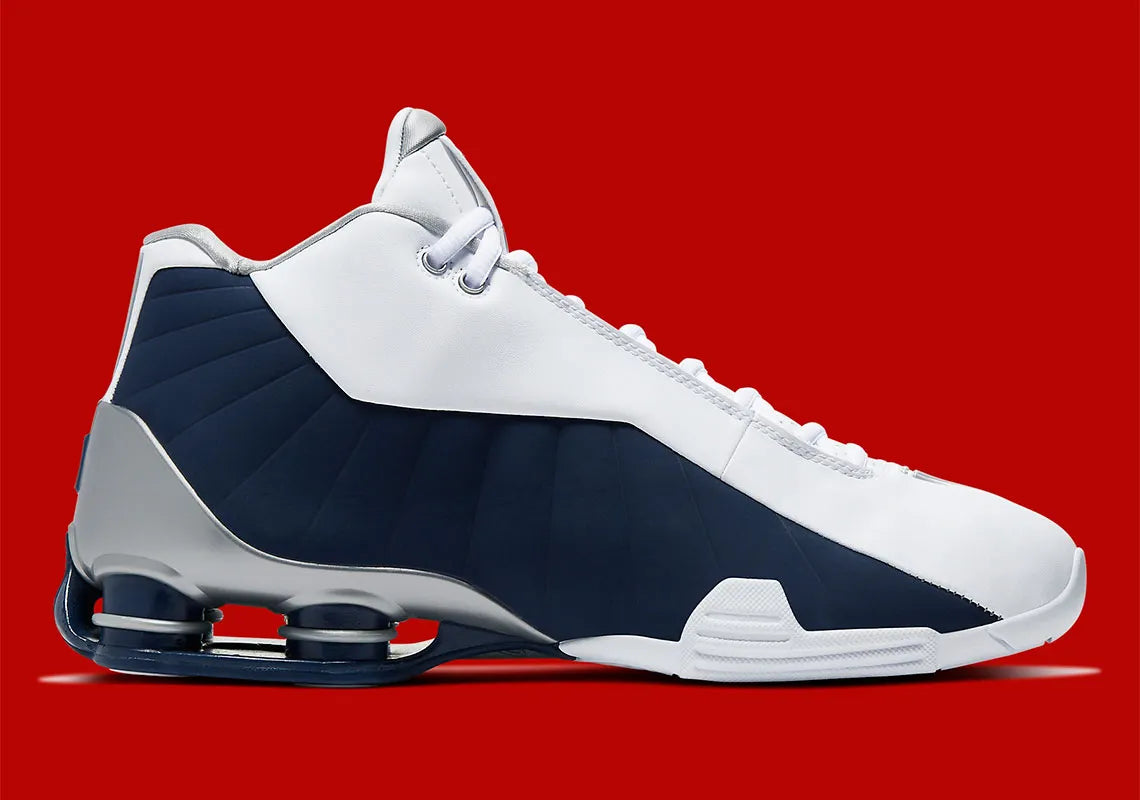 Nike Shox BB4 Olympics avec tige en cuir synthétique blanc et nubuck bleu marine, détails Metallic Silver, amorti Zoom Air à l'avant-pied et quatre colonnes Nike Shox au talon.
