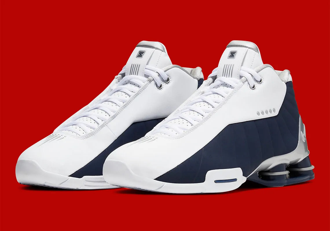 Nike Shox BB4 Olympics avec tige en cuir synthétique blanc et nubuck bleu marine, détails Metallic Silver, amorti Zoom Air à l'avant-pied et quatre colonnes Nike Shox au talon.