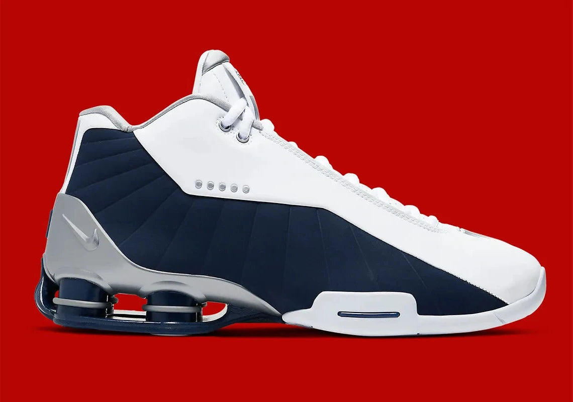 Nike Shox BB4 Olympics avec tige en cuir synthétique blanc et nubuck bleu marine, détails Metallic Silver, amorti Zoom Air à l'avant-pied et quatre colonnes Nike Shox au talon.