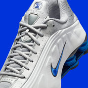 Nike Shox R4 Orlando avec tige en cuir synthétique blanc, détails noirs et bleus, amorti Nike Shox à quatre colonnes et semelle extérieure en caoutchouc.