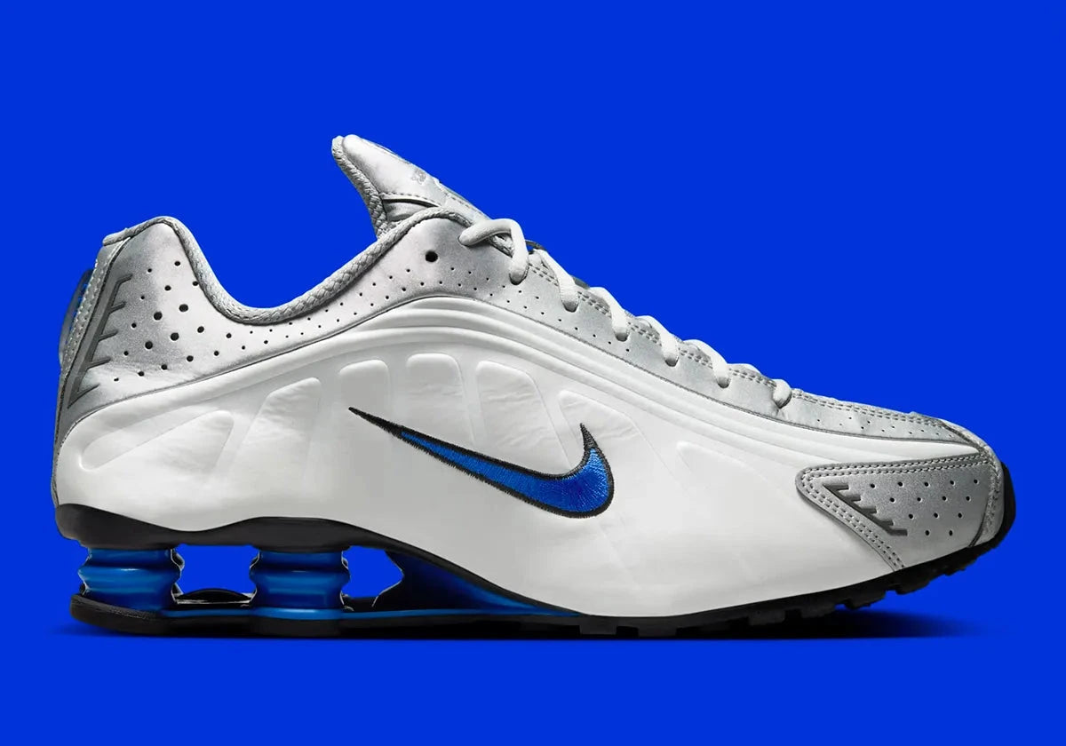 Nike Shox R4 Orlando avec tige en cuir synthétique blanc, détails noirs et bleus, amorti Nike Shox à quatre colonnes et semelle extérieure en caoutchouc.