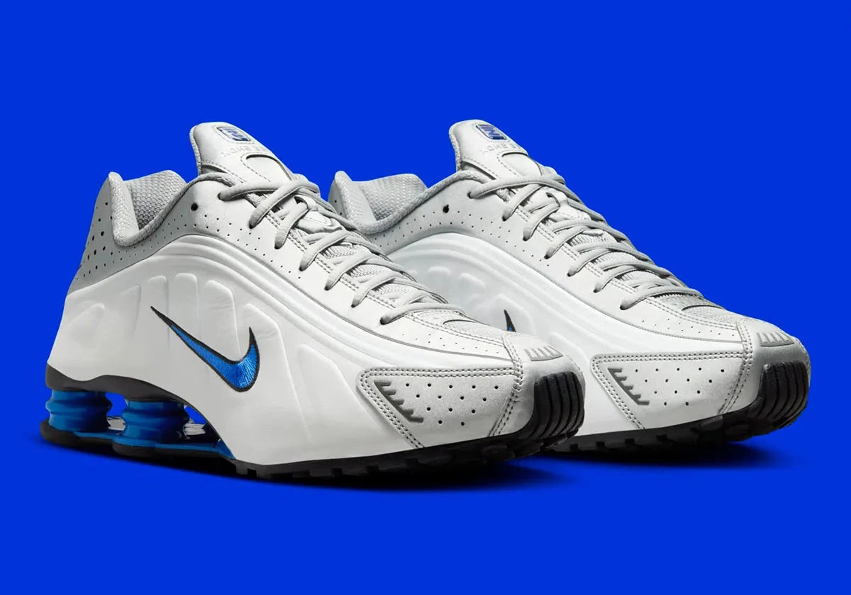 Nike Shox R4 Orlando avec tige en cuir synthétique blanc, détails noirs et bleus, amorti Nike Shox à quatre colonnes et semelle extérieure en caoutchouc.
