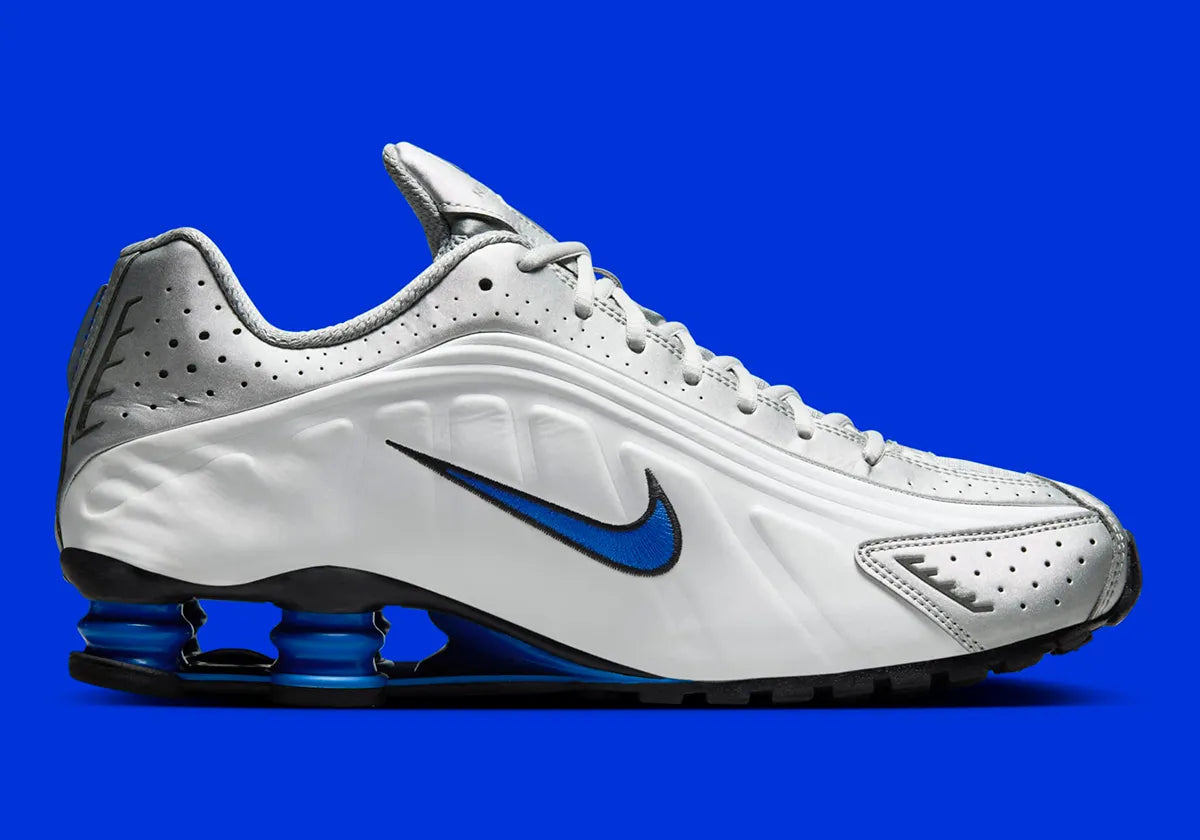 Nike Shox R4 Orlando avec tige en cuir synthétique blanc, détails noirs et bleus, amorti Nike Shox à quatre colonnes et semelle extérieure en caoutchouc.