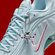 Nike Shox R4 Puerto Rico avec tige Glacier Blue en cuir synthétique, détails University Red et Metallic Silver, graphismes PR, porte-bonheur Vejigante et amorti Nike Shox à quatre colonnes.