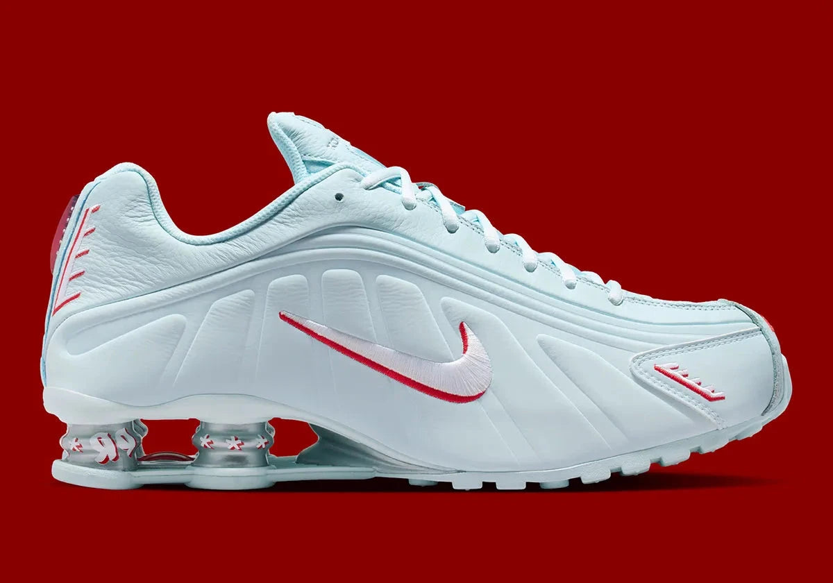 Nike Shox R4 Puerto Rico avec tige Glacier Blue en cuir synthétique, détails University Red et Metallic Silver, graphismes PR, porte-bonheur Vejigante et amorti Nike Shox à quatre colonnes.
