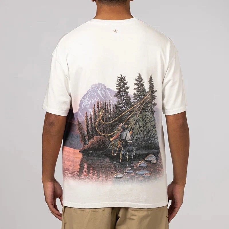 Nike x NOCTA Opal Reels Tee White, tee-shirt blanc en coton avec illustration paysage et pêcheur, détails multicolores et Swoosh orange.