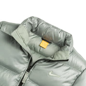 Nike x NOCTA Sunset Puffer Jacket Mica Green, doudoune vert mica métallisé avec matelassage, Swoosh Nike et logo NOCTA.