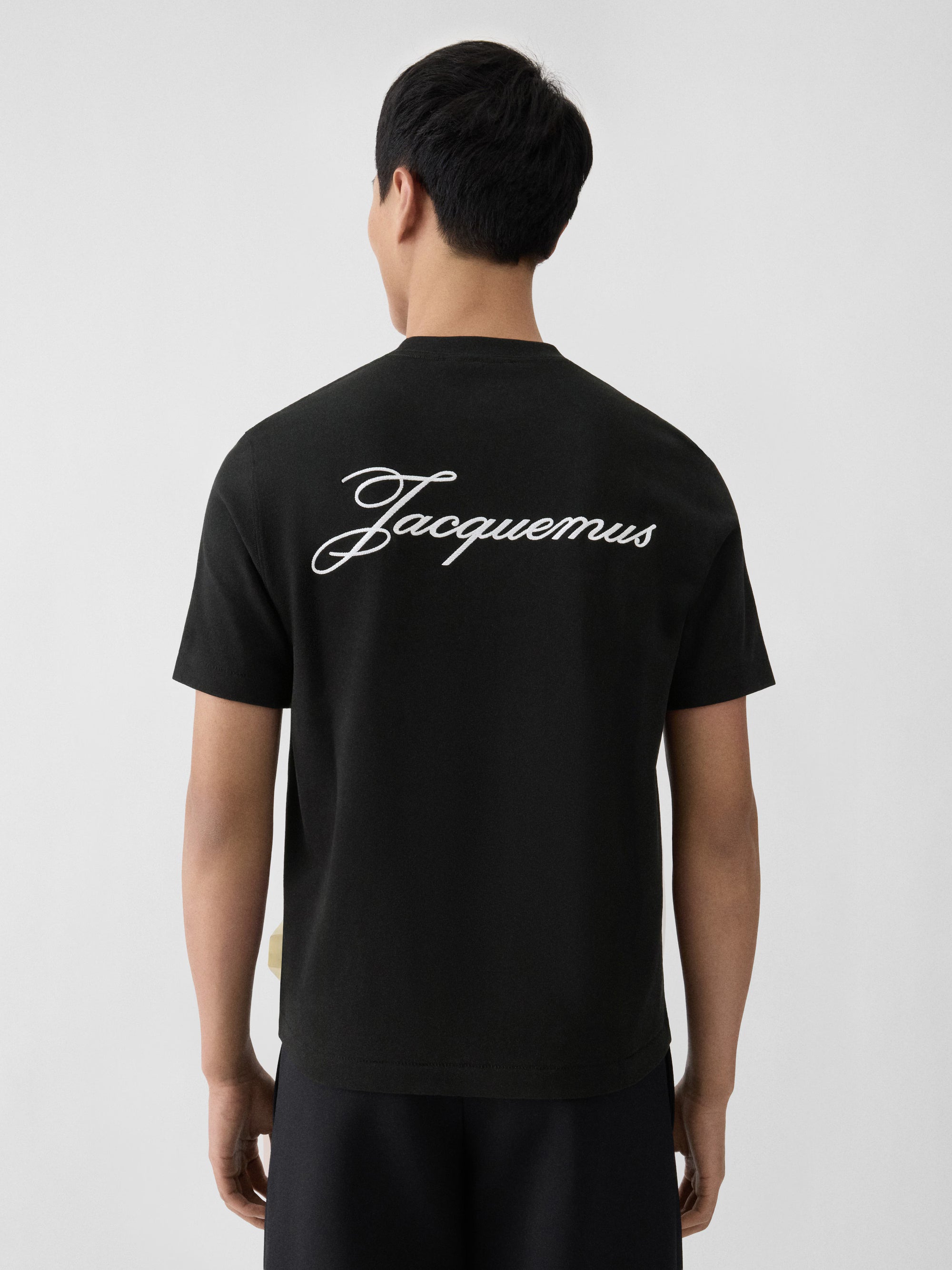 T-shirt Jacquemus en coton noir premium avec logo script blanc, au design minimaliste et élégant.
