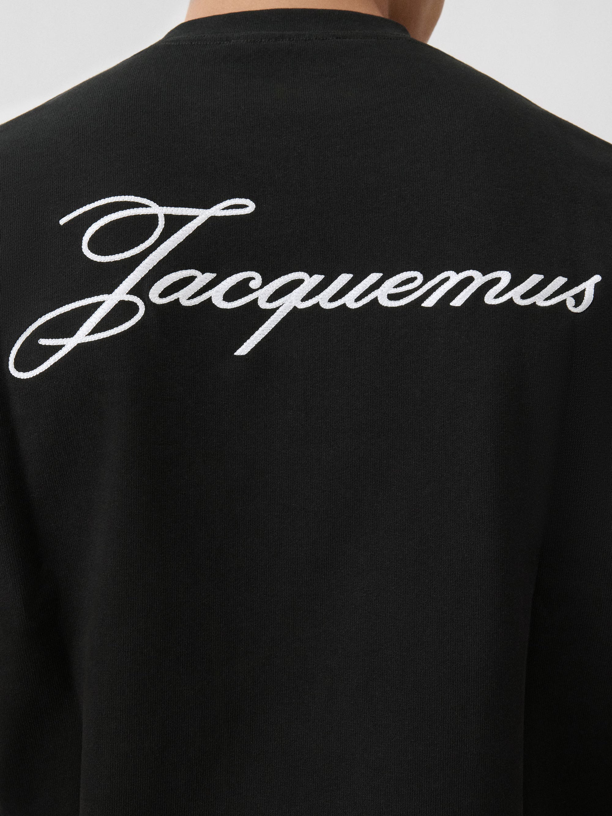 T-shirt Jacquemus en coton noir premium avec logo script blanc, au design minimaliste et élégant.
