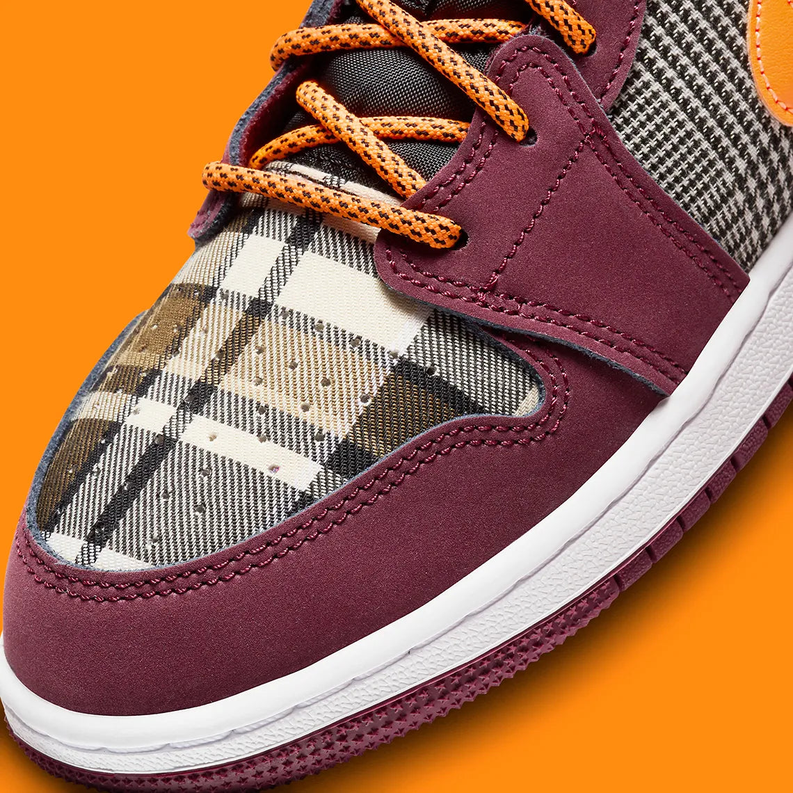 Air Jordan 1 Mid SE Plaid, sneaker mi-montante bordeaux, noire et blanche avec panneaux à carreaux tartan et détails orange.