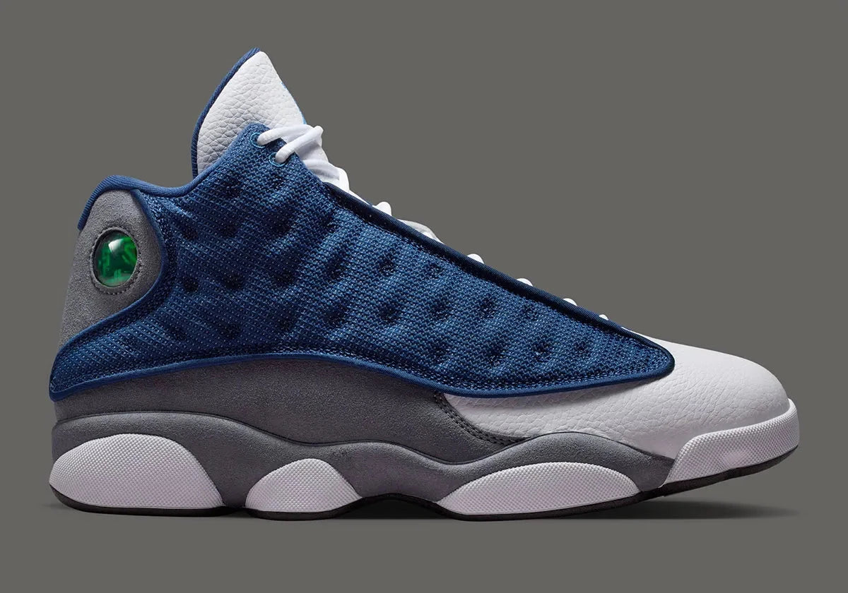 Air Jordan 13 Retro Flint 2026, sneaker Jordan Brand en cuir blanc, mesh réfléchissant bleu marine et suède Flint Grey avec amorti Zoom Air et œil holographique.
