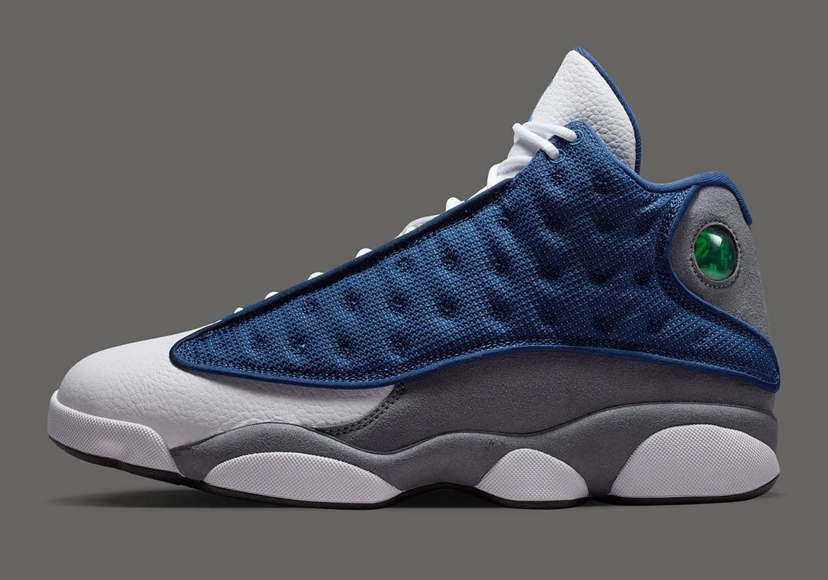 Air Jordan 13 Retro Flint 2026, sneaker Jordan Brand en cuir blanc, mesh réfléchissant bleu marine et suède Flint Grey avec amorti Zoom Air et œil holographique.