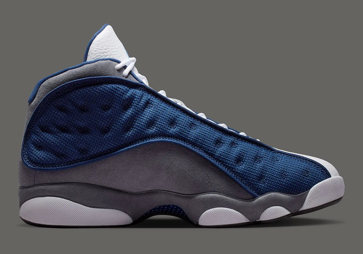Air Jordan 13 Retro Flint 2026, sneaker Jordan Brand en cuir blanc, mesh réfléchissant bleu marine et suède Flint Grey avec amorti Zoom Air et œil holographique.
