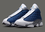 Air Jordan 13 Retro Flint 2026, sneaker Jordan Brand en cuir blanc, mesh réfléchissant bleu marine et suède Flint Grey avec amorti Zoom Air et œil holographique.