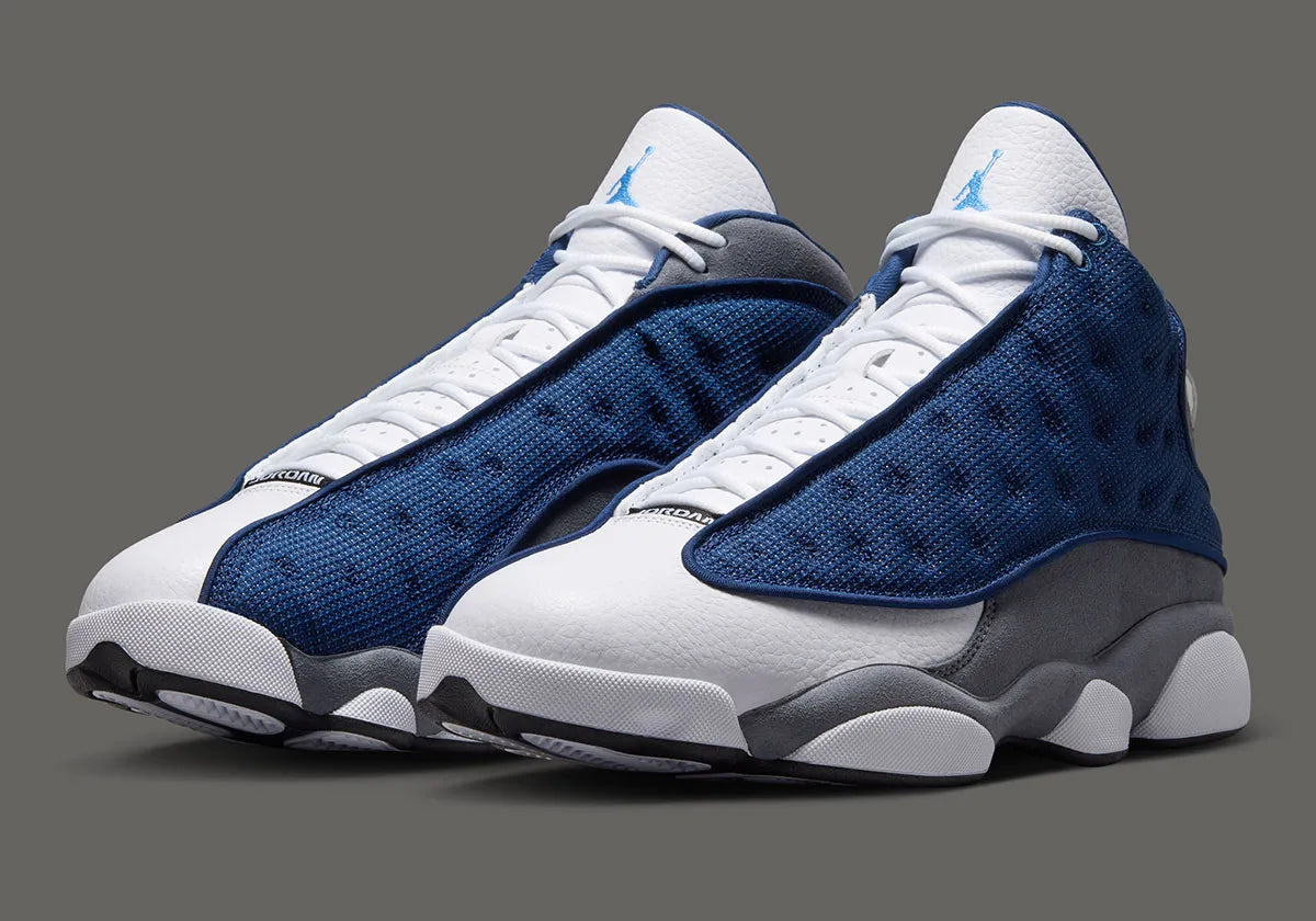 Air Jordan 13 Retro Flint 2026, sneaker Jordan Brand en cuir blanc, mesh réfléchissant bleu marine et suède Flint Grey avec amorti Zoom Air et œil holographique.