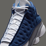 Air Jordan 13 Retro Flint 2026, sneaker Jordan Brand en cuir blanc, mesh réfléchissant bleu marine et suède Flint Grey avec amorti Zoom Air et œil holographique.