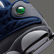 Air Jordan 13 Retro Flint 2026, sneaker Jordan Brand en cuir blanc, mesh réfléchissant bleu marine et suède Flint Grey avec amorti Zoom Air et œil holographique.