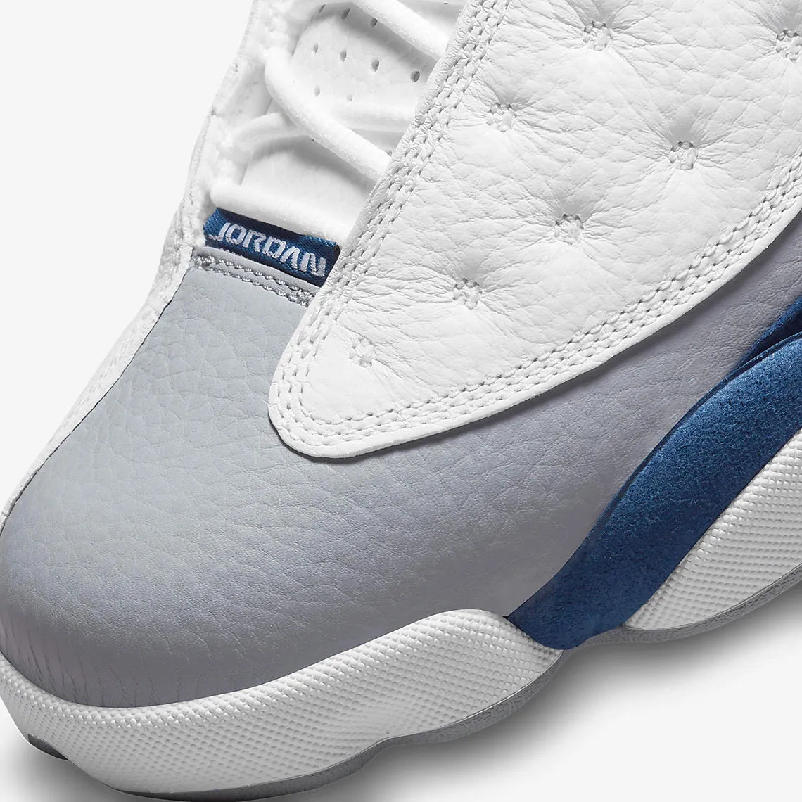 Vue zoomée sur la toe box de la Air Jordan 13 Retro French Blue 414571-164 en cuir blanc avec panneaux French Blue, avant-pied gris, Jumpman rouge et hologramme latéral.