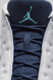 Vue zoomée sur la languette de la Air Jordan 13 Retro Low Hornets 310810-107 en cuir blanc avec empiècements Midnight Navy, accents Turquoise Blue et Jumpman métallique.