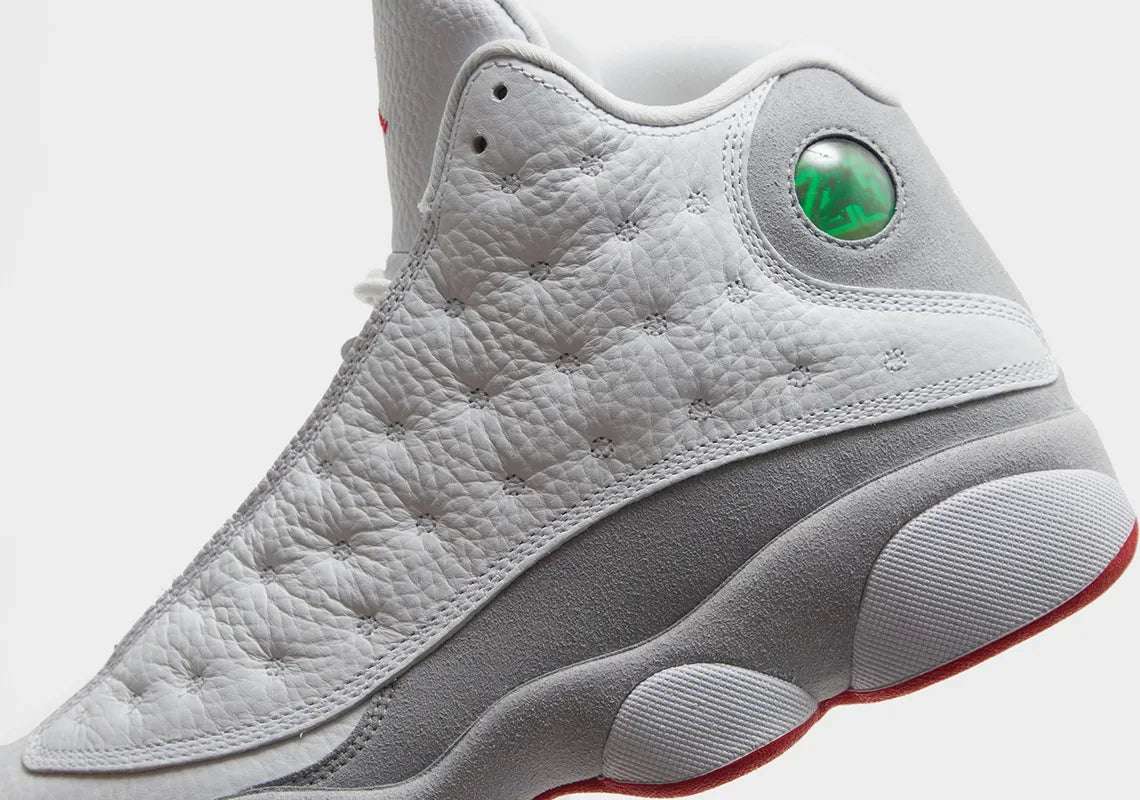 Vue zoomée sur les détails latéraux de la Air Jordan 13 Retro Wolf Grey 414571-160 en cuir blanc avec panneaux Wolf Grey, détails True Red, semelle segmentée et hologramme vert.