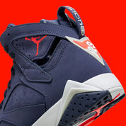 Vue zoomée sur les détails arrières de la Air Jordan 7 Retro Quai 54 2022 DV0577-500 en suède et nubuck bleu marine avec accents Bright Crimson, semelle blanche et branding Quai 54.